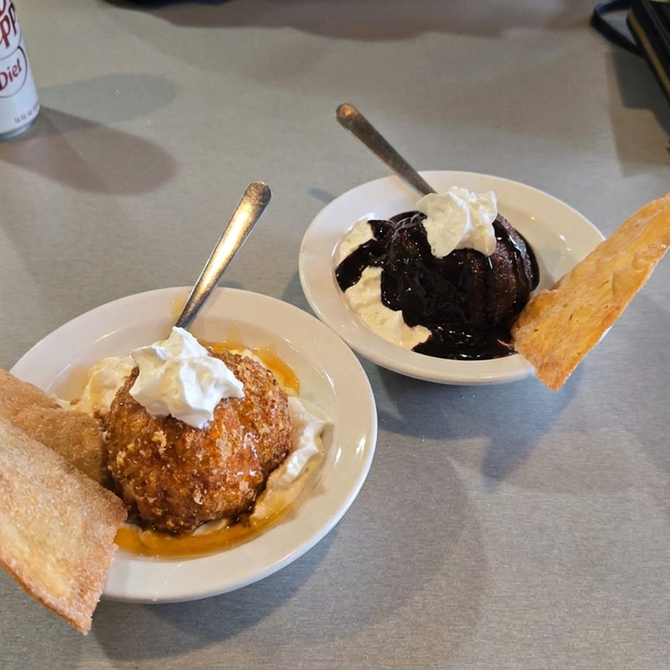 Two dessert bowls topped with whipped cream, syrup, chocolate sauce, and crispy pastry pieces on a restaurant table.
