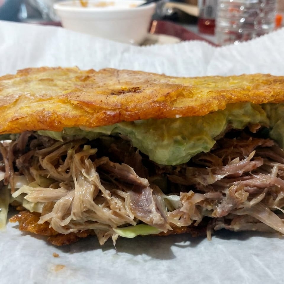Close-up of a crispy golden sandwich filled with shredded meat, lettuce, and creamy green sauce on parchment paper.