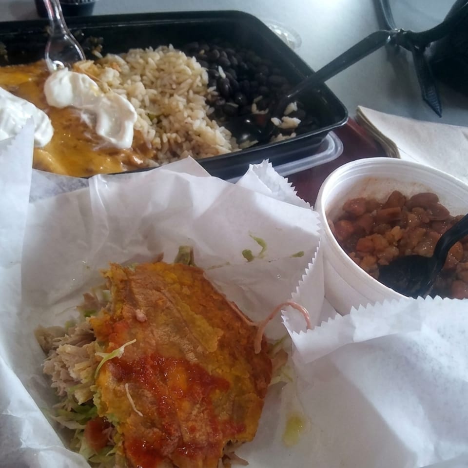 Mexican meal featuring a crispy sauced entrée over rice, beans, and lettuce, with a side of stewed beans and creamy-topped dish.
